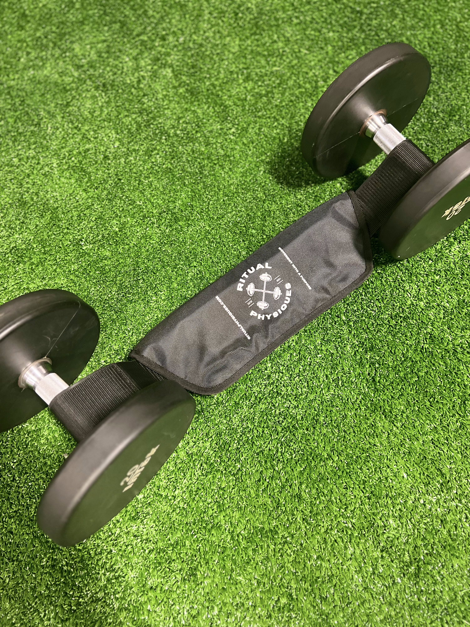 Ritual Physiques' Hip Thrust Belt with attached dumbbells on gym turf.