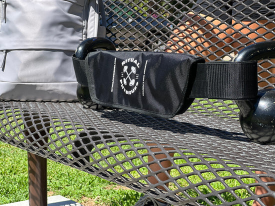 Ritual Physiques' Hip Thrust Belt shown on park bench with kettlebells.